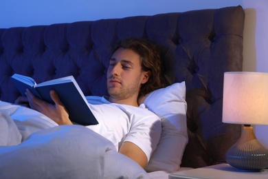 Handsome young man reading book in dark room at night. Bedtime