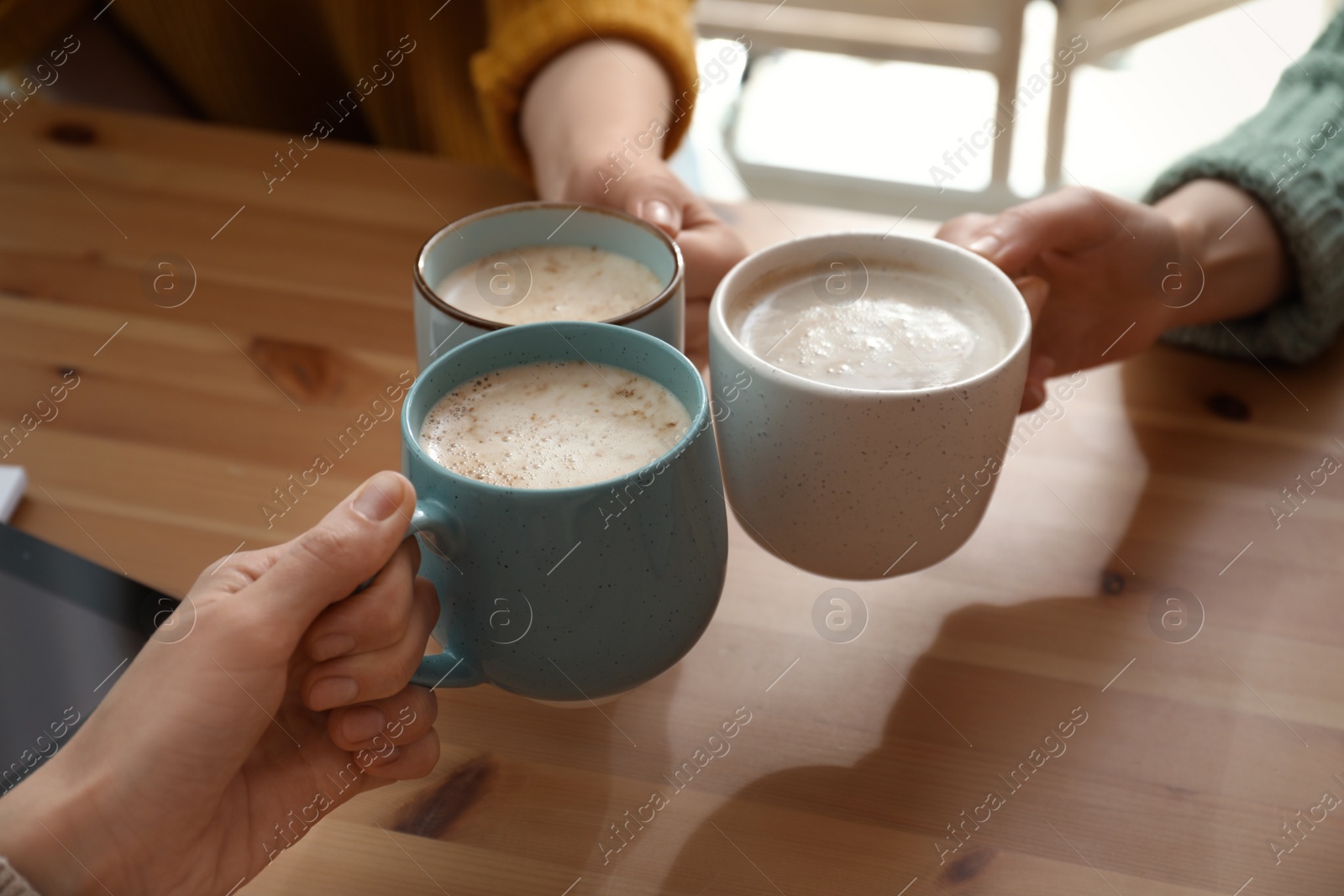 Photo of Women clinking cups of coffee at table in cafe, closeup