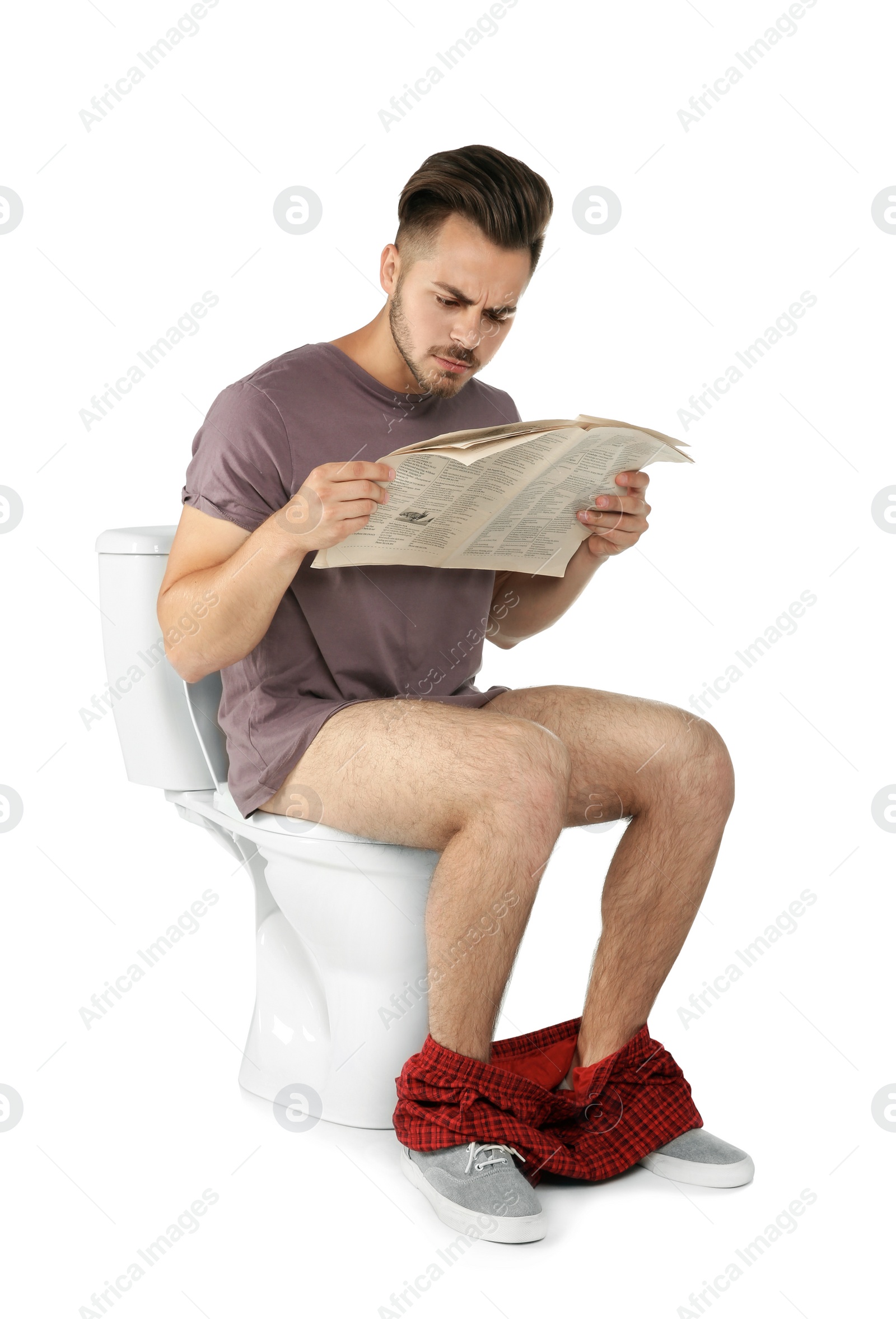 Photo of Young man reading newspaper while sitting on toilet bowl. Isolated on white