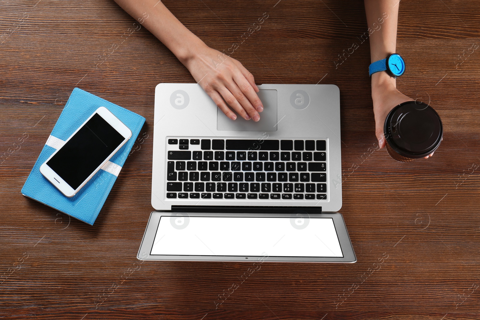 Photo of Young woman holding coffee while using laptop at wooden table, top view