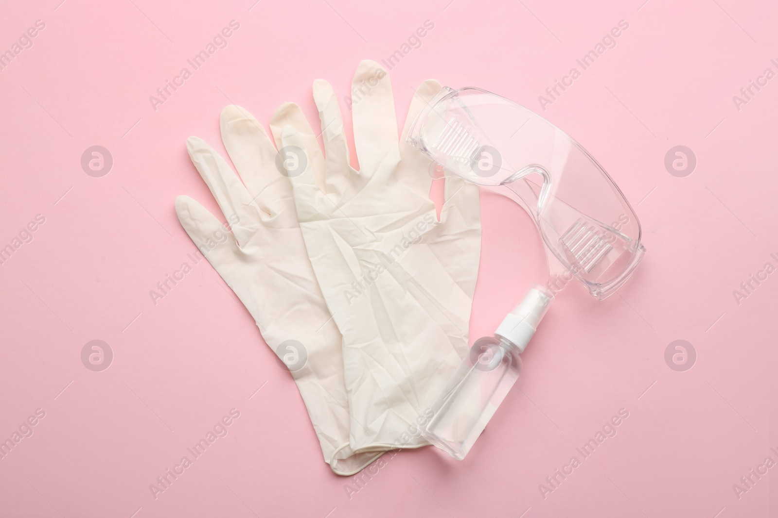 Photo of Medical gloves, goggles and hand sanitizer on pink background, flat lay