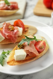 Photo of Plate of tasty bruschettas with prosciutto on table