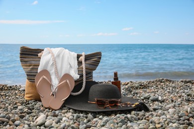 Photo of Beautiful hat with sunglasses, bag and flip flops near sea on pebble beach. Space for text