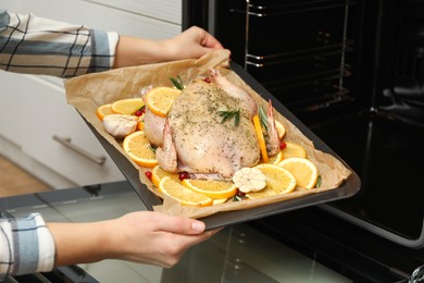 Photo of Woman putting chicken with orange slices into oven, closeup