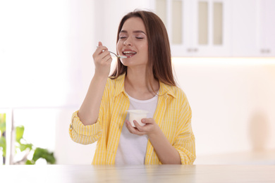 Young attractive woman eating tasty yogurt at table in kitchen