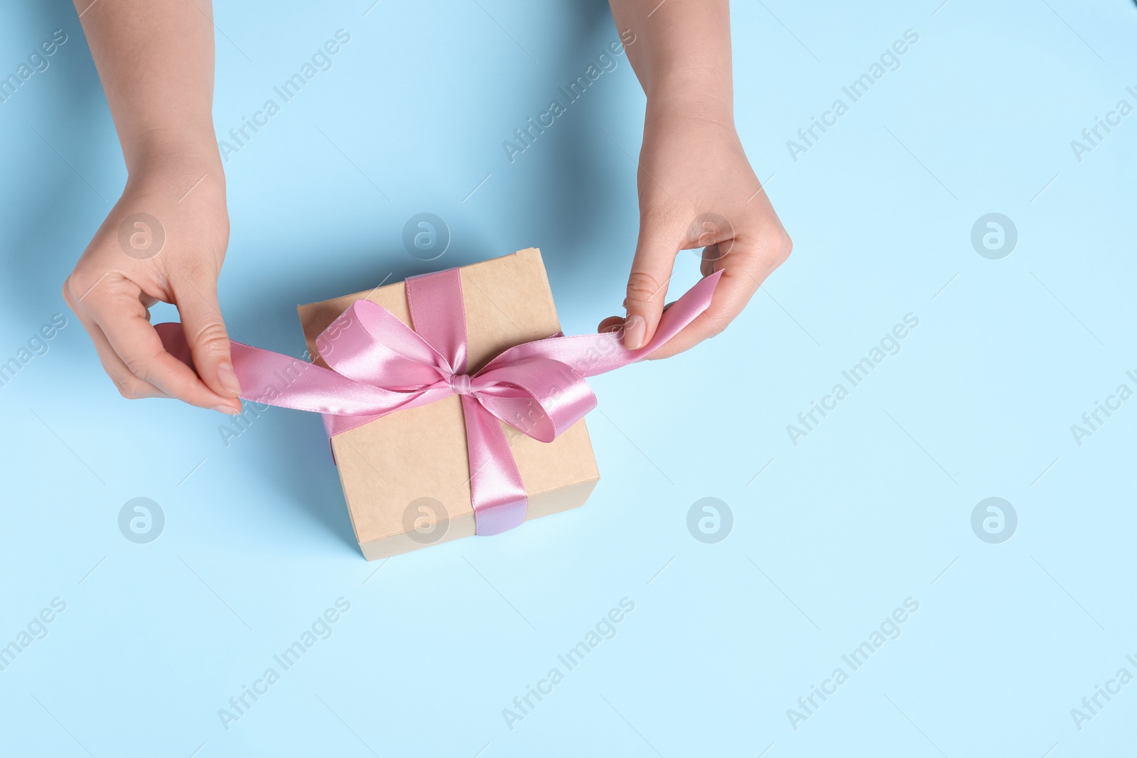 Photo of Woman with gift box on light blue background, top view. Space for text