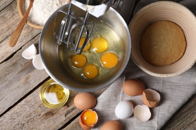 Photo of Making dough. Raw eggs in bowl of stand mixer and ingredients on wooden table, flat lay