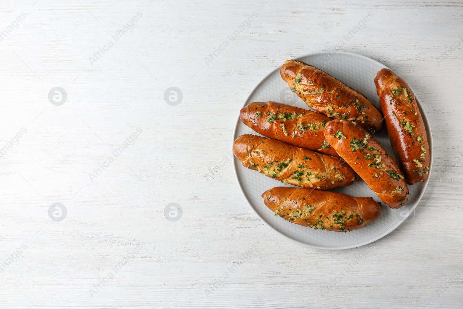 Photo of Plate of bread loaves with garlic and herbs on white wooden table, top view. Space for text