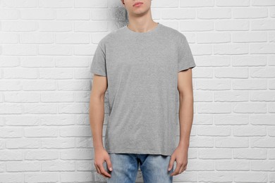 Man wearing gray t-shirt near white brick wall, closeup. Mockup for design