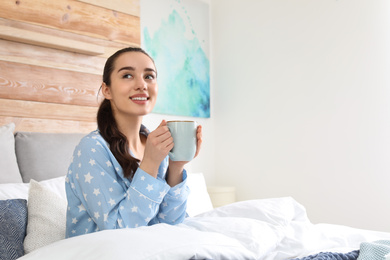 Photo of Woman with cup of hot drink in large bed at home. Elegant interior