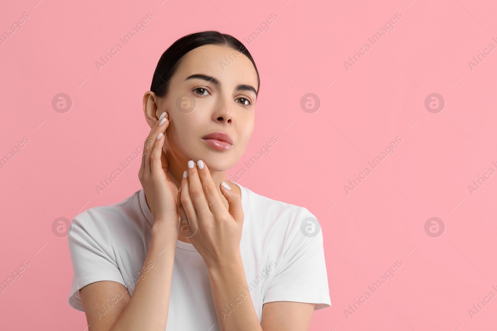 Photo of Woman with dry skin checking her face on pink background, space for text