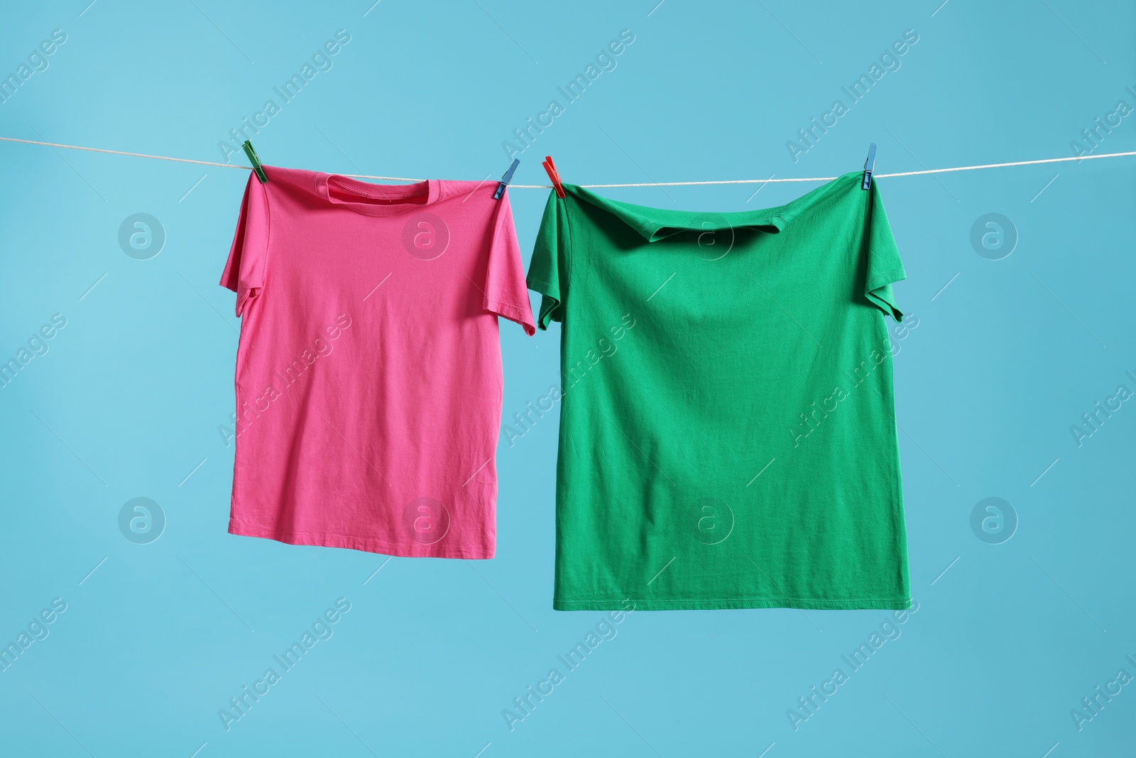 Photo of Two colorful t-shirts drying on washing line against light blue background
