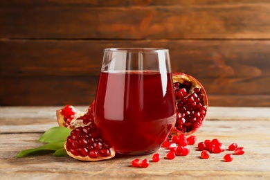 Photo of Glass of pomegranate juice and fresh fruits on table against wooden background