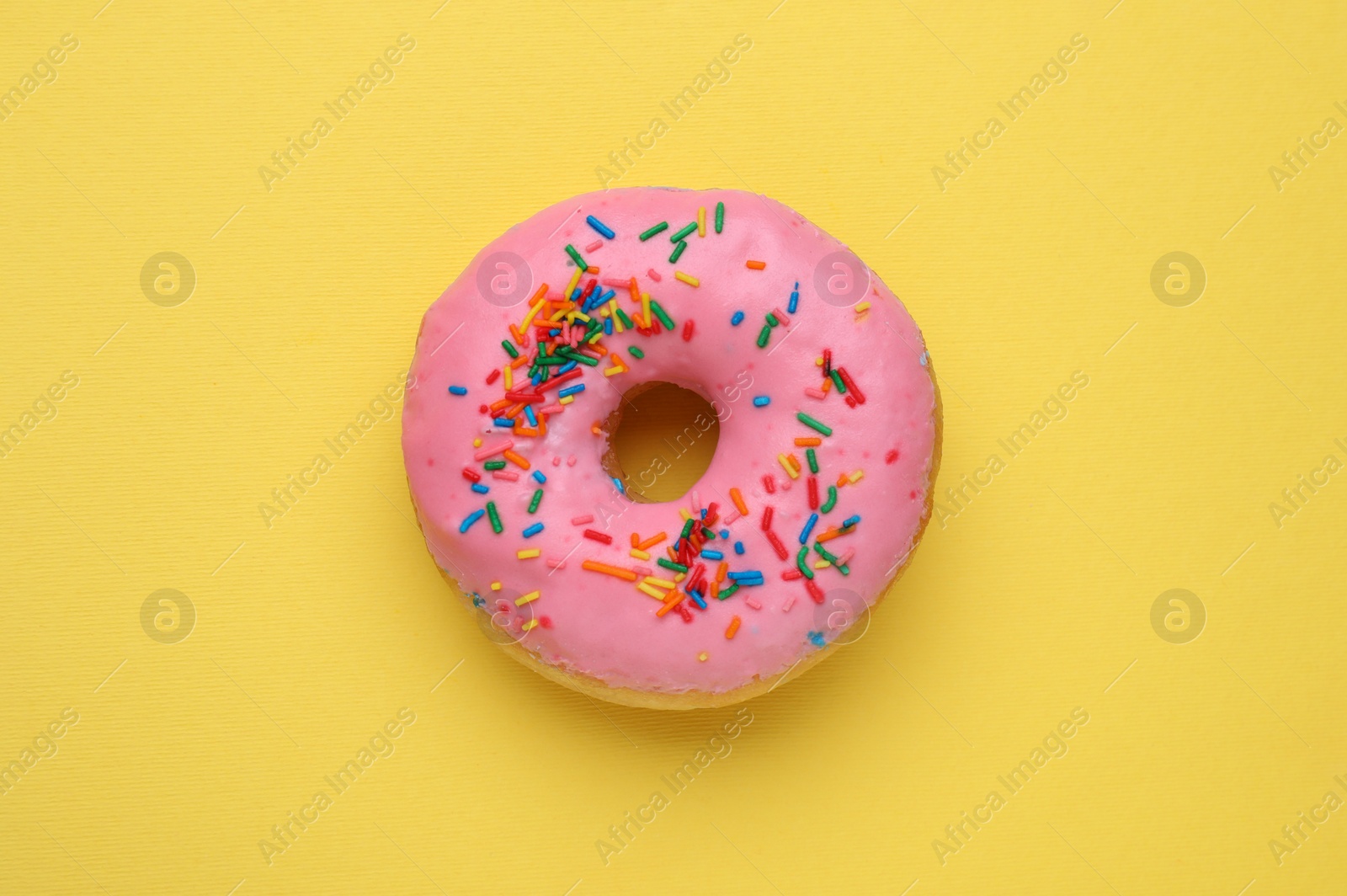 Photo of Tasty glazed donut decorated with sprinkles on yellow background, top view