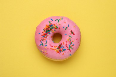Photo of Tasty glazed donut decorated with sprinkles on yellow background, top view