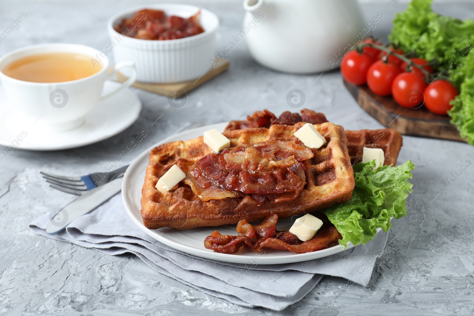 Photo of Delicious Belgium waffles served with fried bacon and butter on grey table
