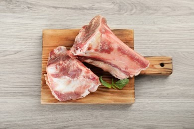 Photo of Cutting board with raw chopped meaty bones and basil on wooden table, top view