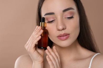 Beautiful young woman with bottle of essential oil on brown background