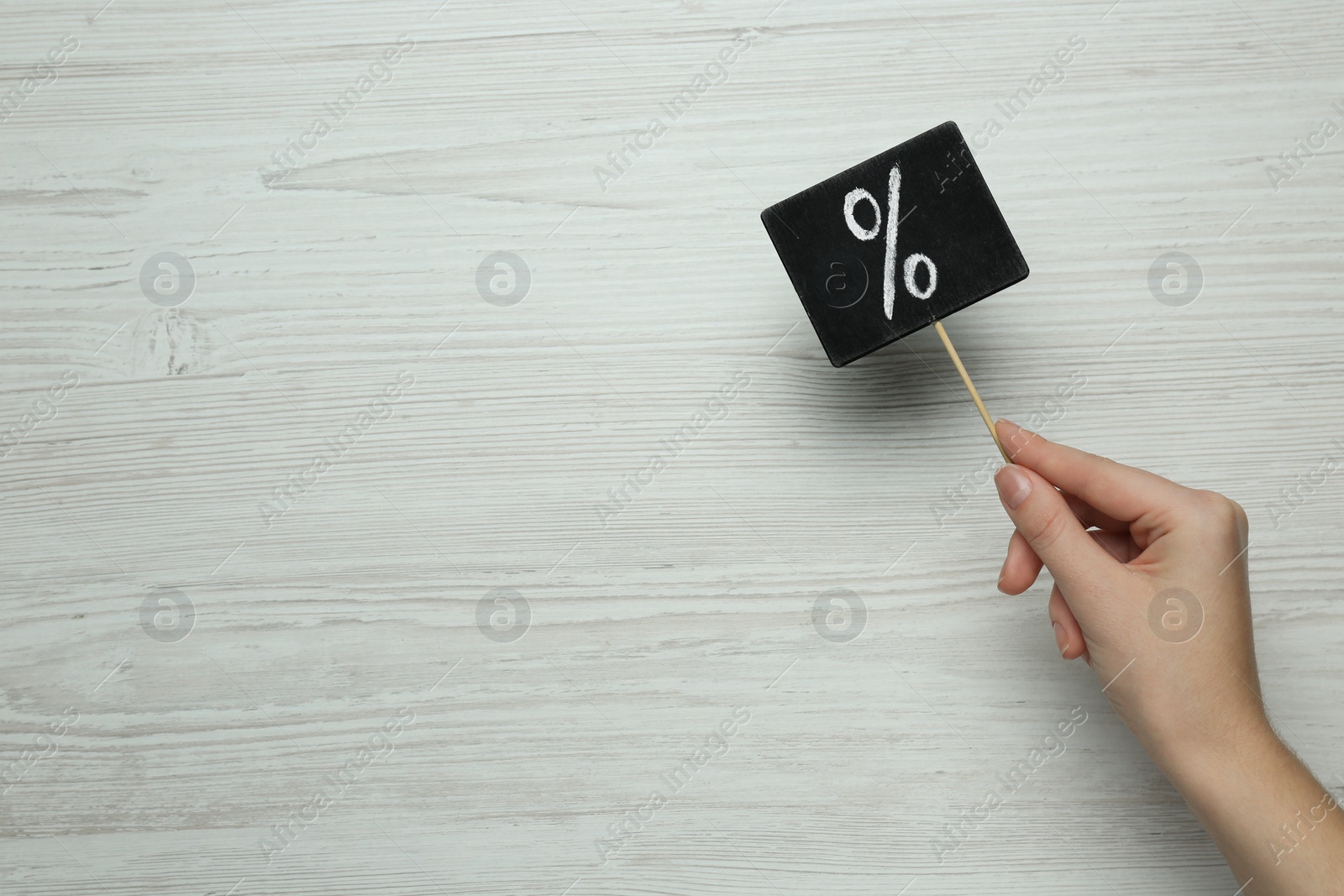 Photo of Woman holding sign with percent symbol at white wooden table, top view. Space for text