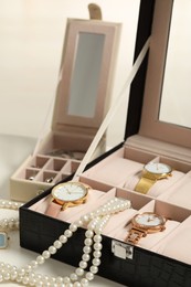 Photo of Jewelry boxes with many stylish wristwatches, accessories and pearl necklace on white table, closeup