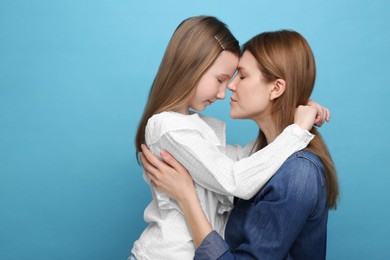 Portrait of mother and her cute daughter on light blue background. Space for text