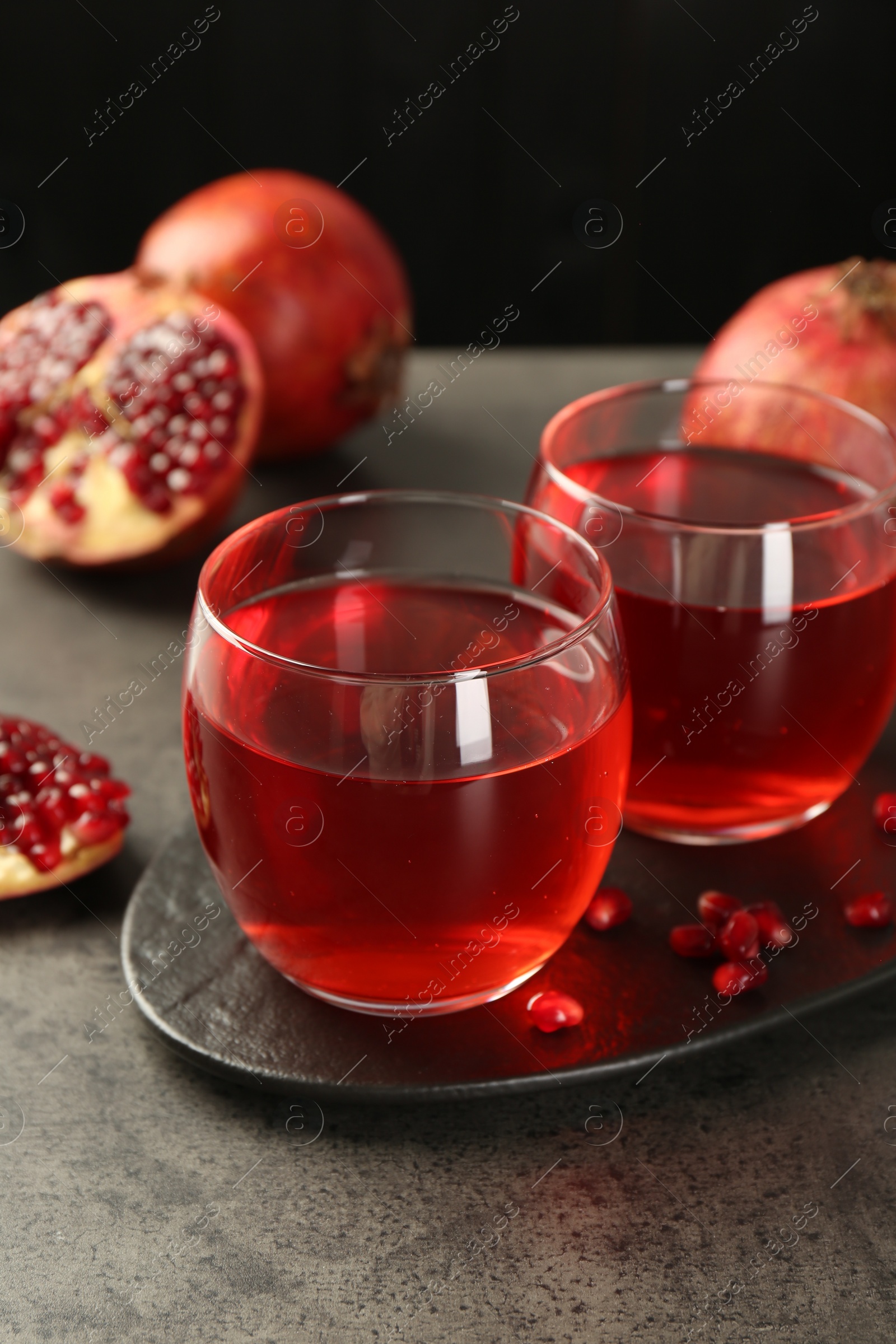 Photo of Tasty pomegranate juice in glasses and fresh fruits on grey table, closeup