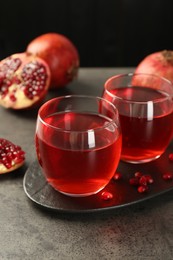 Photo of Tasty pomegranate juice in glasses and fresh fruits on grey table, closeup