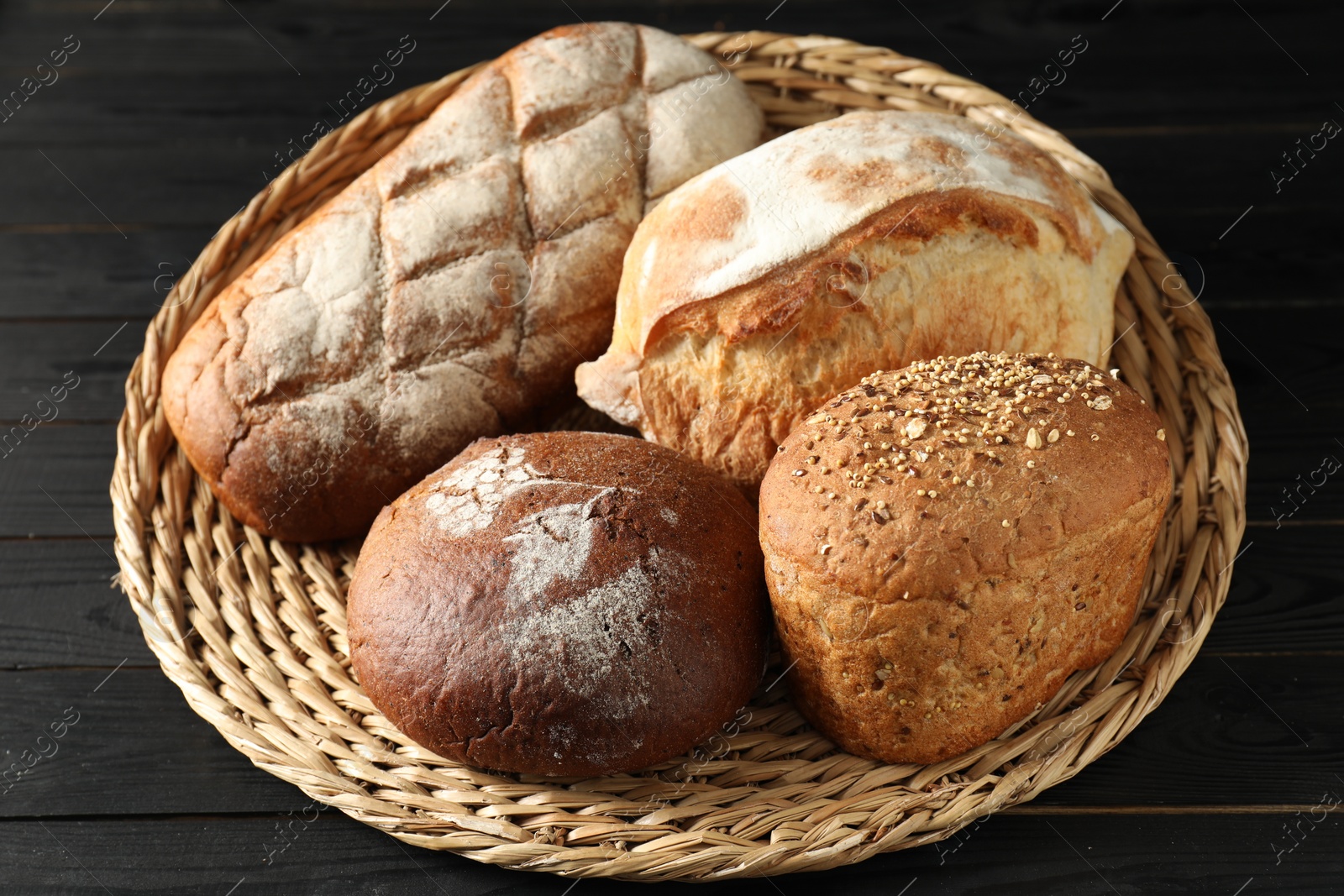 Photo of Wicker basket with different types of fresh bread on black wooden table