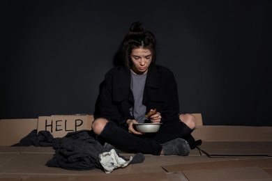 Photo of Poor woman with bread sitting on floor near dark wall