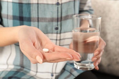 Woman holding pill and glass of water indoors, closeup