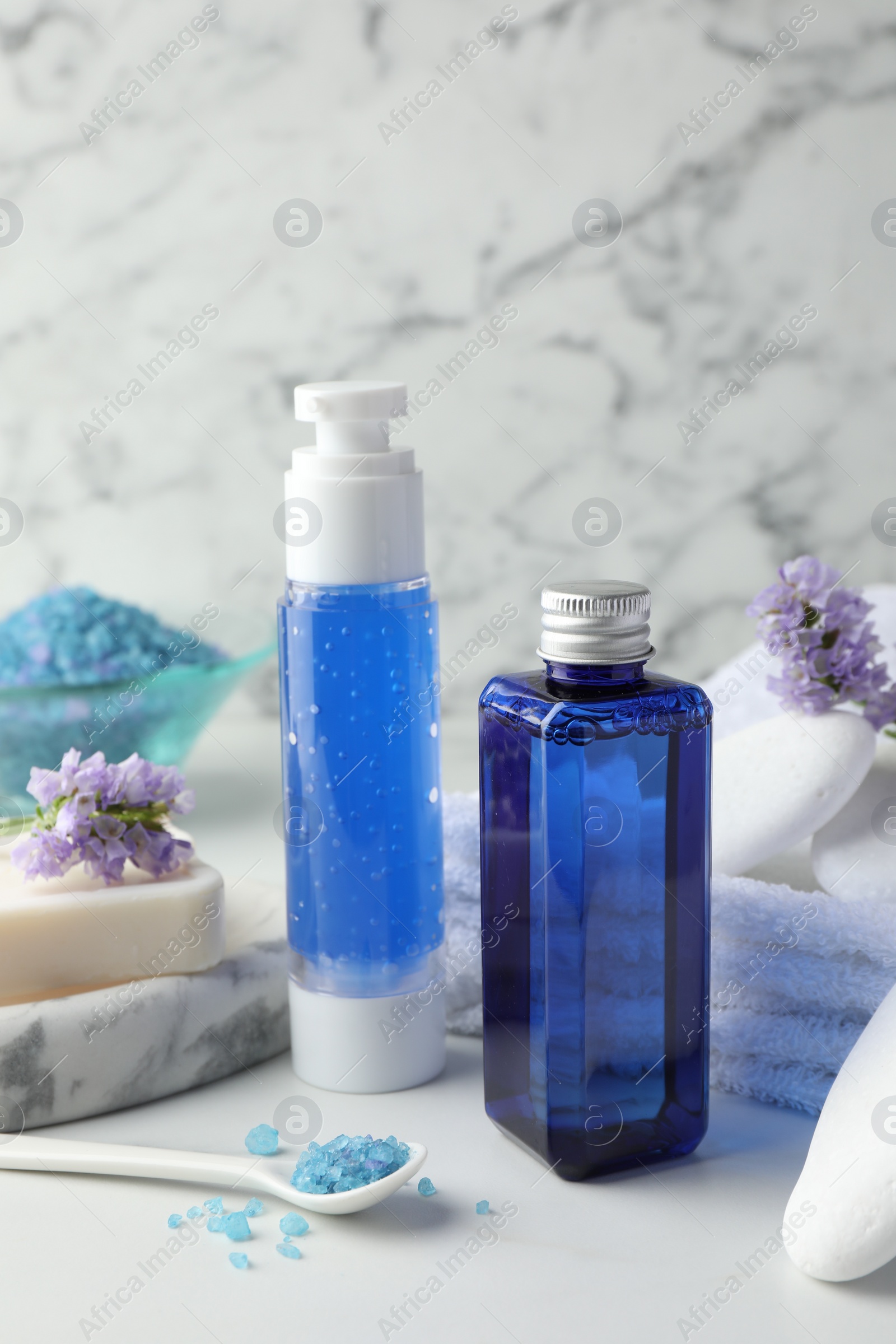 Photo of Spa composition. Bottles of cosmetic products, sea salt, stones, soap and flowers on white table