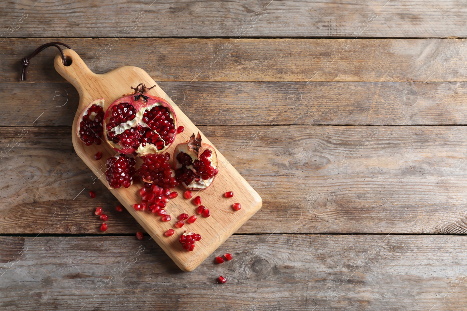 Photo of Board with ripe pomegranates and seeds on wooden background, top view. Space for text