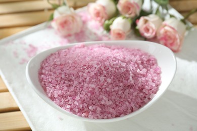 Bowl with pink sea salt on wooden table, closeup