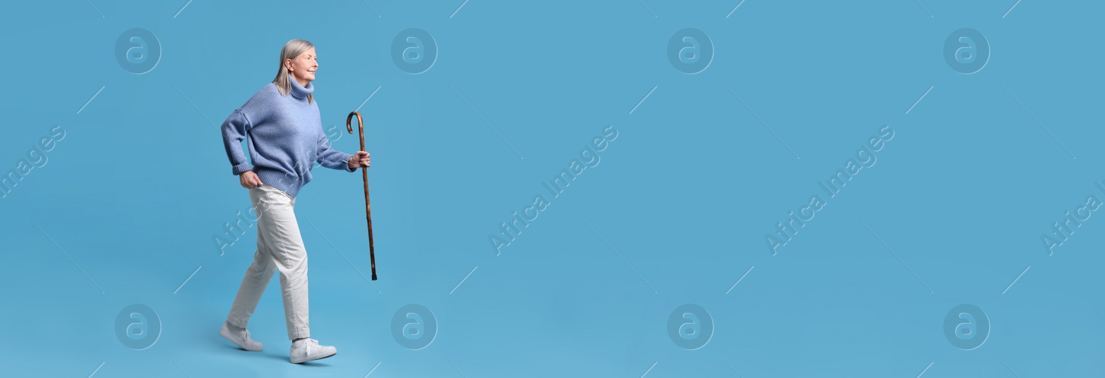 Image of Senior woman with walking cane on light blue background. Banner design with space for text