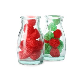 Delicious gummy raspberry candies in glass bottles on white background