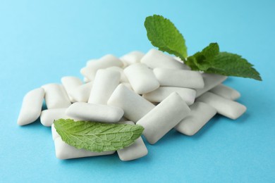 Pile of tasty white chewing gums and mint leaves on light blue background, closeup