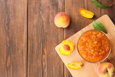 Flat lay composition with bowl of tasty peach jam and fresh fruit on wooden table