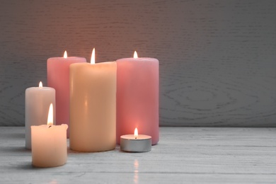 Different wax candles burning on table against light background