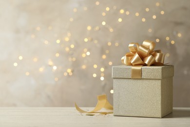 Photo of Beautiful golden gift box on light table against blurred festive lights, space for text