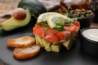 Delicious salmon tartare served with avocado, sauce and croutons on table, closeup