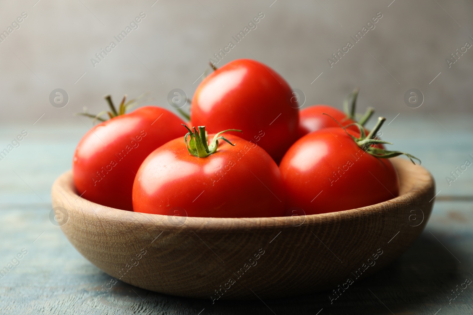 Photo of Ripe tomatoes in bowl on blue wooden table, closeup