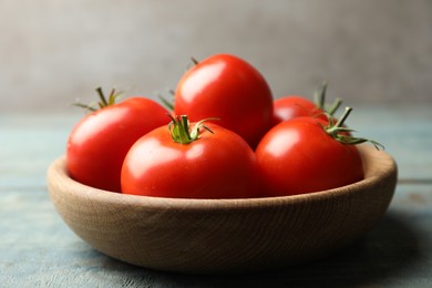 Photo of Ripe tomatoes in bowl on blue wooden table, closeup