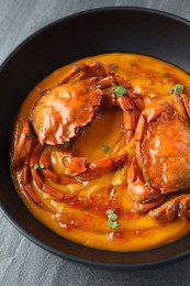 Delicious boiled crabs with sauce in bowl on grey table, closeup