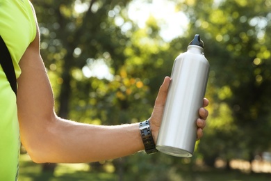 Photo of Young man holding bottle of water in park on sunny day, closeup