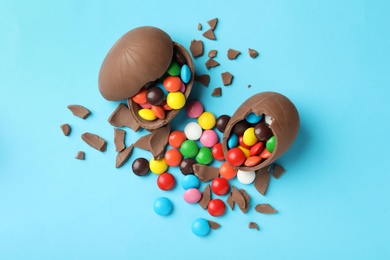 Photo of Broken chocolate eggs with candies on light blue background, flat lay