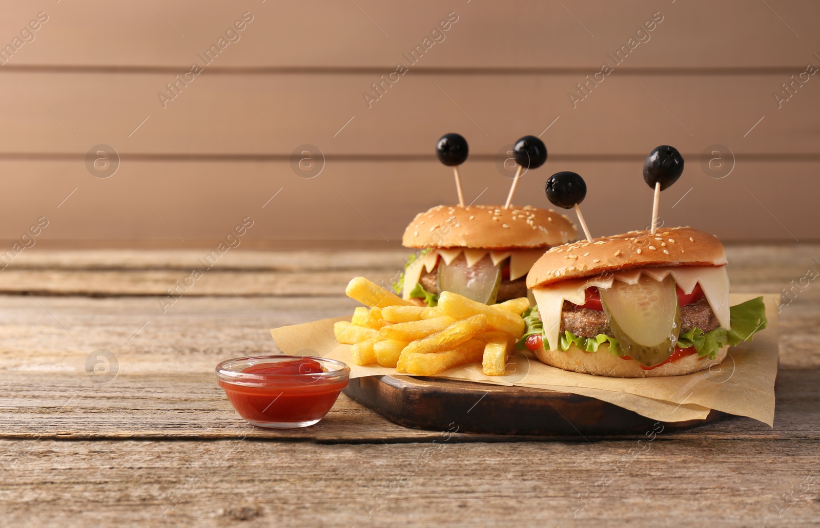 Photo of Cute monster burgers served with french fries and ketchup on wooden table, space for text. Halloween party food