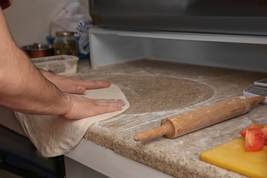 Photo of Man preparing dough for pizza at table, closeup. Oven recipe
