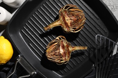 Photo of Pan with tasty grilled artichokes on table, flat lay