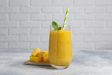 Photo of Glass of tasty pineapple smoothie and cut fruit on light gray table
