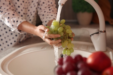 Woman washing fresh grapes in kitchen sink, closeup